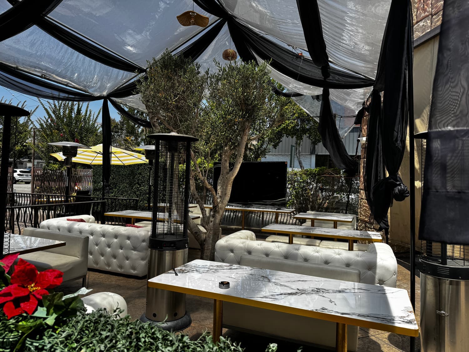 Phoenicia patio lounge with tufted sofas, marble tables, and an olive tree under a draped canopy
